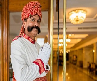 Indian Concierge, Doorman dressed in traditional indian clothes welcomes the guest at the entrance with the typical indian welcome gesture and a happy smile. Agra, India.